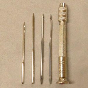 May include: A set of five silver-toned tools for leather crafting. The set includes a hand drill with a textured grip and four different sized awls.