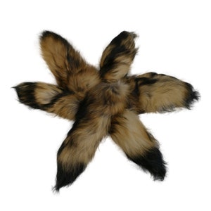 May include: Five brown and black fox tails arranged in a star shape. The tails are fluffy and soft.