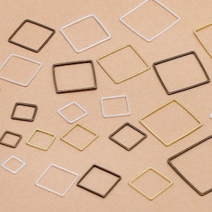 Könnte beinhalten: Sortiment quadratischer Metallrahmen in Silber, Gold und Bronze. Die Rahmen sind in verschiedenen Größen und auf einer hellbraunen Oberfläche angeordnet.