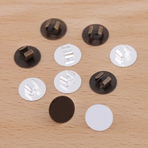 May include: Assortment of round metal blanks with a clip on the back. Some blanks are silver, some are bronze, and some are black.