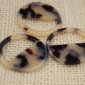 May include: Three tortoiseshell plastic rings with a half-circle cut out. The rings are cream and brown with a mottled pattern.