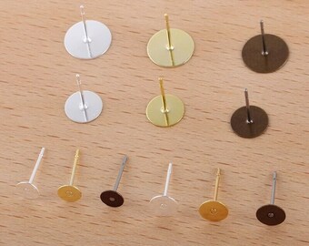 May include: Assortment of earring blanks in silver, gold, and bronze. The blanks are round and have a flat back with a post for attaching earrings.