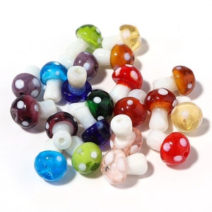 Op de afbeelding: Een verzameling kleurrijke glazen paddenstoel kralen met witte stippen. De kralen zijn allemaal in verschillende kleuren, waaronder rood, blauw, groen, paars en oranje. Ze zijn perfect voor het maken van sieraden of andere knutselwerkjes.