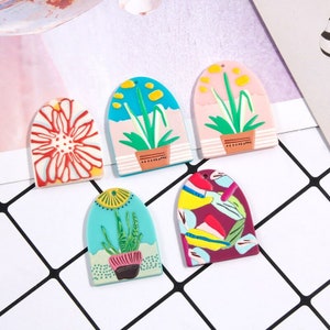 May include: Five colorful arched resin charms with different floral and plant designs. The charms are perfect for adding a touch of whimsy to jewelry, keychains, or other crafts.