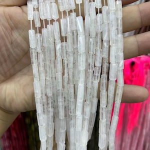 May include: A collection of translucent, clear, rectangular tube-shaped beads strung together on multiple thin white threads. The beads have a smooth, polished surface and a consistent cylindrical form, creating a vertical arrangement of light-reflecting segments.