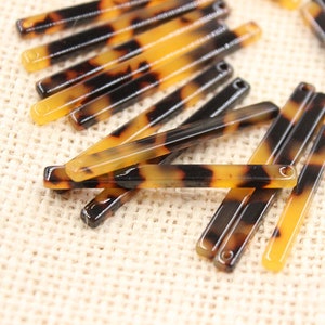 May include: A group of brown and black tortoiseshell hair barrettes with a shiny finish. The barrettes are arranged in a random pattern on a beige fabric surface.