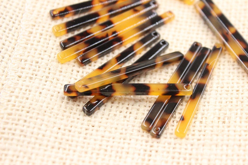 May include: A group of brown and black tortoiseshell hair barrettes with a shiny finish. The barrettes are arranged in a random pattern on a beige fabric surface.