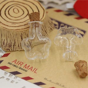 Puede incluir: Dos botellas de vidrio transparente con tapones de corcho en forma de estrellas. Las botellas est&aacute;n sobre una superficie de papel marr&oacute;n con el texto "AIR MAIL 00180/2000".