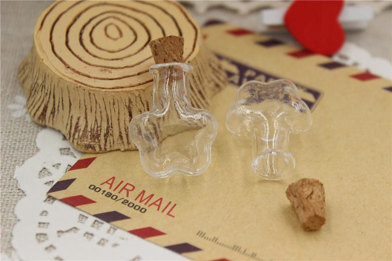 Puede incluir: Dos botellas de vidrio transparente con tapones de corcho en forma de estrellas. Las botellas est&aacute;n sobre una superficie de papel marr&oacute;n con el texto "AIR MAIL 00180/2000".