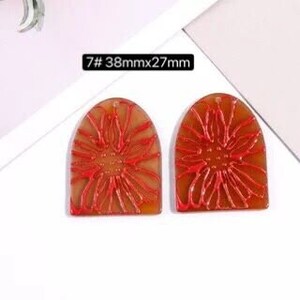 May include: Two brown and red resin flower-shaped earrings with a rounded top. The earrings are approximately 38 mm by 27 mm.