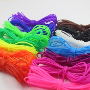 Puede incluir: Surtido de cordones elásticos de colores en varios colores brillantes, incluyendo morado, azul, verde, amarillo, naranja, rojo, rosa, blanco, negro y marrón. Los cordones están dispuestos en forma de semicírculo.