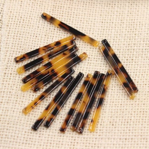 Puede incluir: Una colección de doce barrettes para el cabello de color marrón y negro de caparazón de tortuga. Las barrettes están dispuestas en forma de abanico sobre un fondo de tela beige.