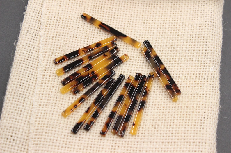 May include: A collection of twelve brown and black tortoiseshell hair barrettes. The barrettes are arranged in a fan shape on a beige fabric background.