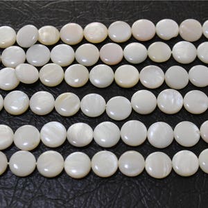 May include: A strand of white mother of pearl beads. The beads are round and flat, and they have a smooth, polished finish.
