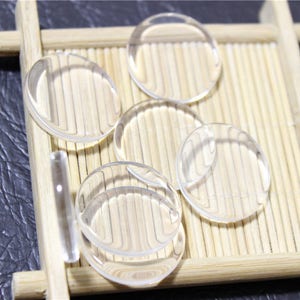 May include: Five clear round glass cabochons, approximately 2.5 cm in diameter, are arranged on a bamboo mat.