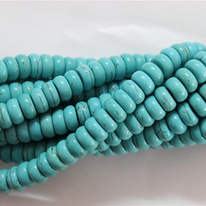 May include: A strand of turquoise beads, each bead is a light blue color with brown veining. The beads are round and have a smooth, polished finish.