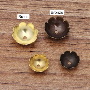 May include: Four scalloped metal bead caps in two colors: brass and bronze. The caps are shown on a wooden surface.