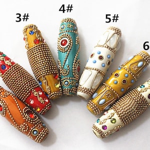 May include: Seven colourful glass beads with gold accents and rhinestones. Each bead has a unique design and is numbered 1 through 7.