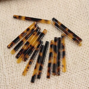 May include: A group of 14 brown and black tortoiseshell hair barrettes. The barrettes are arranged in a pile on a beige hessian surface.