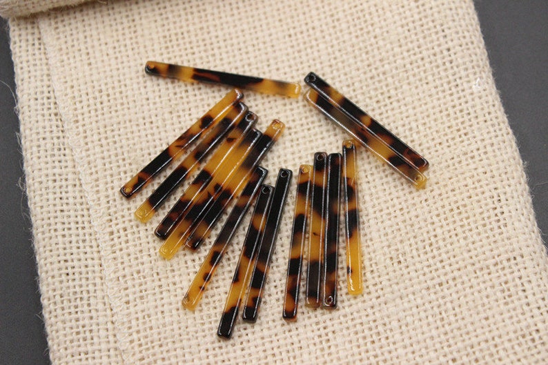 May include: A group of 14 brown and black tortoiseshell hair barrettes. The barrettes are arranged in a pile on a beige hessian surface.
