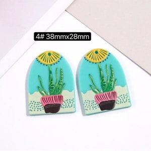 May include: A pair of turquoise blue earrings with a plant design. The earrings are 38mm by 28mm and feature a yellow sun, green plant, and pink pot.