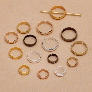 May include: Assortment of 15 gold, silver, and bronze rings with a small clear rhinestone on each ring. The rings are different sizes and have a smooth, polished finish.