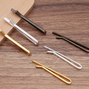 Può includere: Cinque fermagli per cravatta in diverse finiture: oro, argento e bronzo. I fermagli per cravatta sono tutti della stessa dimensione e forma, con un design semplice ed elegante.
