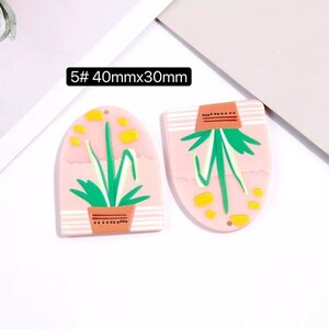 May include: Two pink resin earrings with a plant design. The earrings are 40mm x 30mm and have a hole at the top for hanging.