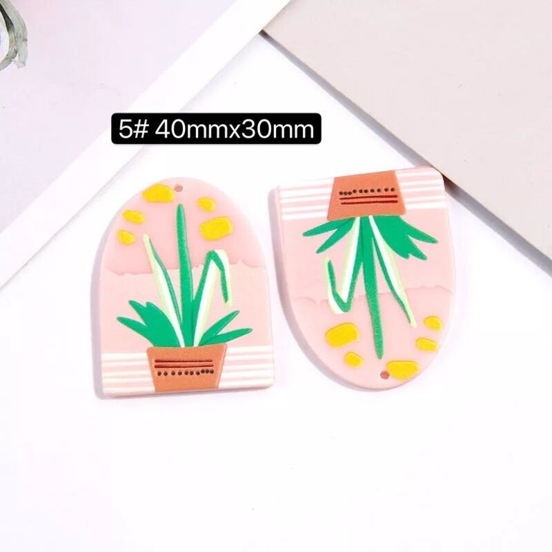 May include: Two pink resin earrings with a plant design. The earrings are 40mm x 30mm and have a hole at the top for hanging.