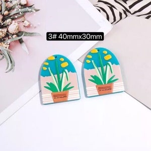 May include: Two blue and pink arched resin earrings with a plant design. The earrings are 40mm x 30mm.