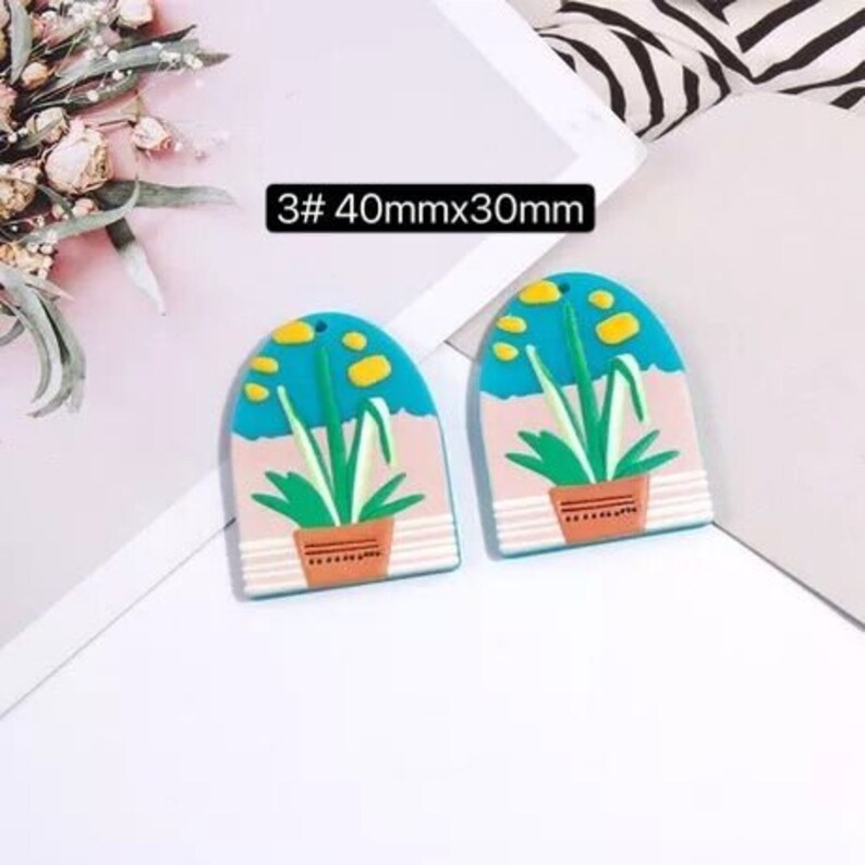 May include: Two blue and pink arched resin earrings with a plant design. The earrings are 40mm x 30mm.