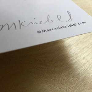May include: A white card with the signature "M. Kriegel" and the website "marcellakriegel.com" printed in silver.