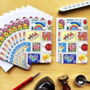 May include: A collection of colorful greeting cards with a stamp-like design featuring rainbows, roses, and the word "LOVE." The cards are arranged on a wooden surface, alongside envelopes, a pen, and a wax seal.