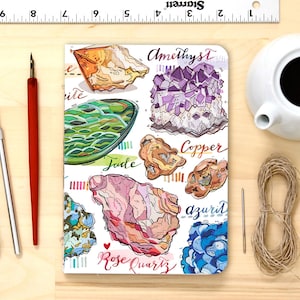 May include: A white notebook cover featuring colourful illustrations of various crystals and their names, including amethyst, copper, jade, azurite, and rose quartz.