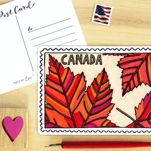 May include: A rectangular sticker featuring a stylised postage stamp design with the word CANADA printed at the top. The design displays vibrant red, orange, and pink maple leaves against a cream background, framed by a black scalloped border.