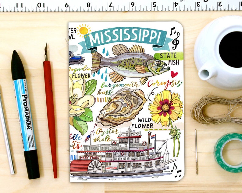 Peut inclure: Un carnet illustr&eacute; blanc avec une banni&egrave;re bleue qui dit "MISSISSIPPI" et pr&eacute;sente diverses illustrations de choses associ&eacute;es &agrave; l'&Eacute;tat, notamment un achigan &agrave; grande bouche, une fleur de magnolia, une coquille d'hu&icirc;tre, un bateau &agrave; vapeur &agrave; roue &agrave; aubes et une fleur sauvage. Le texte "STATE FISH" est &eacute;crit dans le coin sup&eacute;rieur droit du carnet.