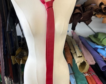 Peut inclure: Une cravate en cuir rouge vif nouée avec un nœud simple autour du cou d'un mannequin buste de couleur crème. La cravate présente une finition lisse et mate ainsi qu'une pointe classique, tombant droit au centre du buste de présentation.