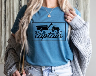Op de afbeelding: Een blauw T-shirt met een zwarte afbeelding van een tractor die een graanwagen trekt. De tekst "GRAIN CART captain" staat onder de afbeelding.