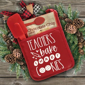 Pode incluir: Luva de forno vermelha com o texto "Teachers bake smart cookies" em branco. Um pacote de mistura para biscoitos de chocolate e uma espátula vermelha estão guardados no bolso da luva.