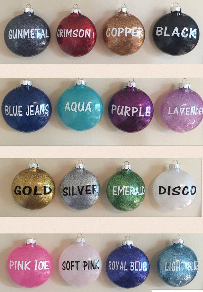 Op de afbeelding: Een verzameling van 16 ronde kerstballen met glitterafwerking. De ballen zijn versierd met verschillende kleuren en woorden, waaronder gunmetal, crimson, copper, black, blue jeans, aqua, purple, lavender, gold, silver, emerald, disco, pink ice, soft pink, royal blue en light blue.