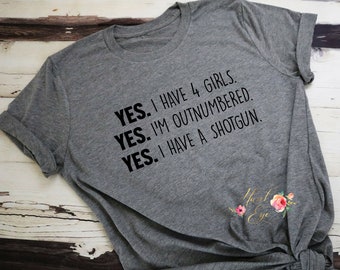 May include: A heather gray t-shirt with the text "YES. I HAVE 4 GIRLS. YES. I'M OUTNUMBERED. YES. I HAVE A SHOTGUN." in black. The shirt has rolled-up sleeves and a floral logo in the bottom right corner.