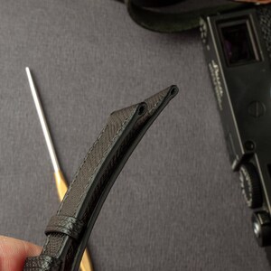 May include: Close-up of a black leather watch strap with stitching detail. The strap is folded in half, showing the underside.