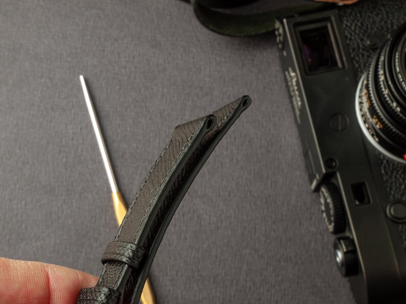 May include: Close-up of a black leather watch strap with stitching detail. The strap is folded in half, showing the underside.