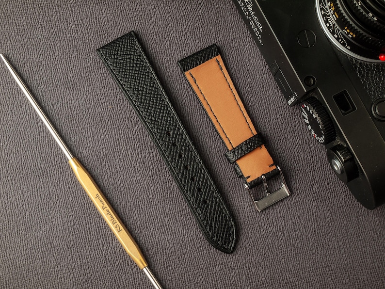 May include: Two watch straps, one black and one brown, with a stitching detail. The straps are laid out on a gray textured surface.