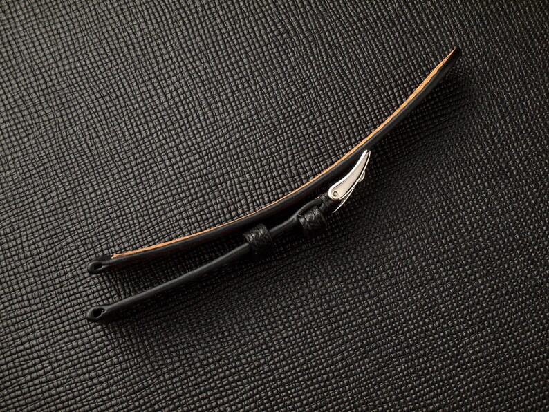 May include: Black leather watch strap with a silver buckle.