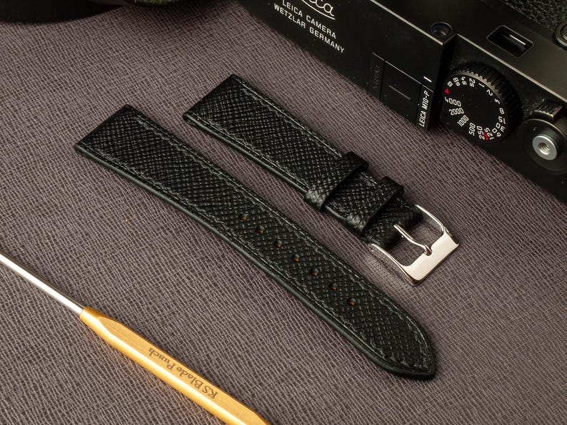 May include: Two black leather watch straps with a silver buckle. The straps have a textured grain pattern.