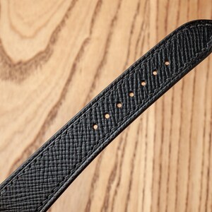 May include: Black leather watch strap with stitching and holes for attaching to a watch.