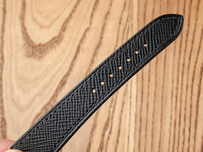 May include: Black leather watch strap with stitching and holes for attaching to a watch.