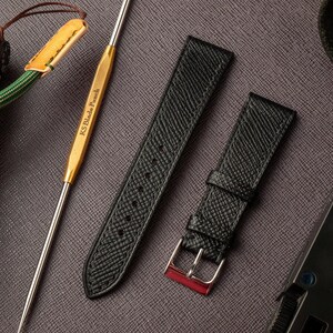 May include: Two black leather watch straps with a textured finish. The strap on the left has a pointed end, while the strap on the right has a buckle with a red accent.