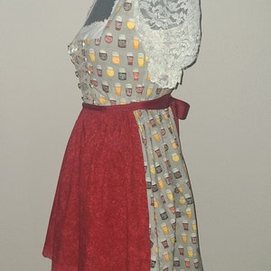 Op de afbeelding: Een grijs en wit dirndl met een rode rok en een kantboord. Het boord is versierd met een patroon van bierglazen. De rok heeft een kantbies.
